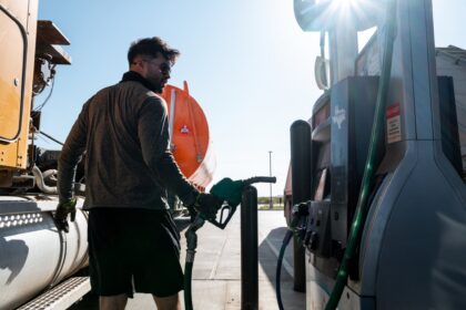 Man fueling a large truck at a gas station with a Texas sticker