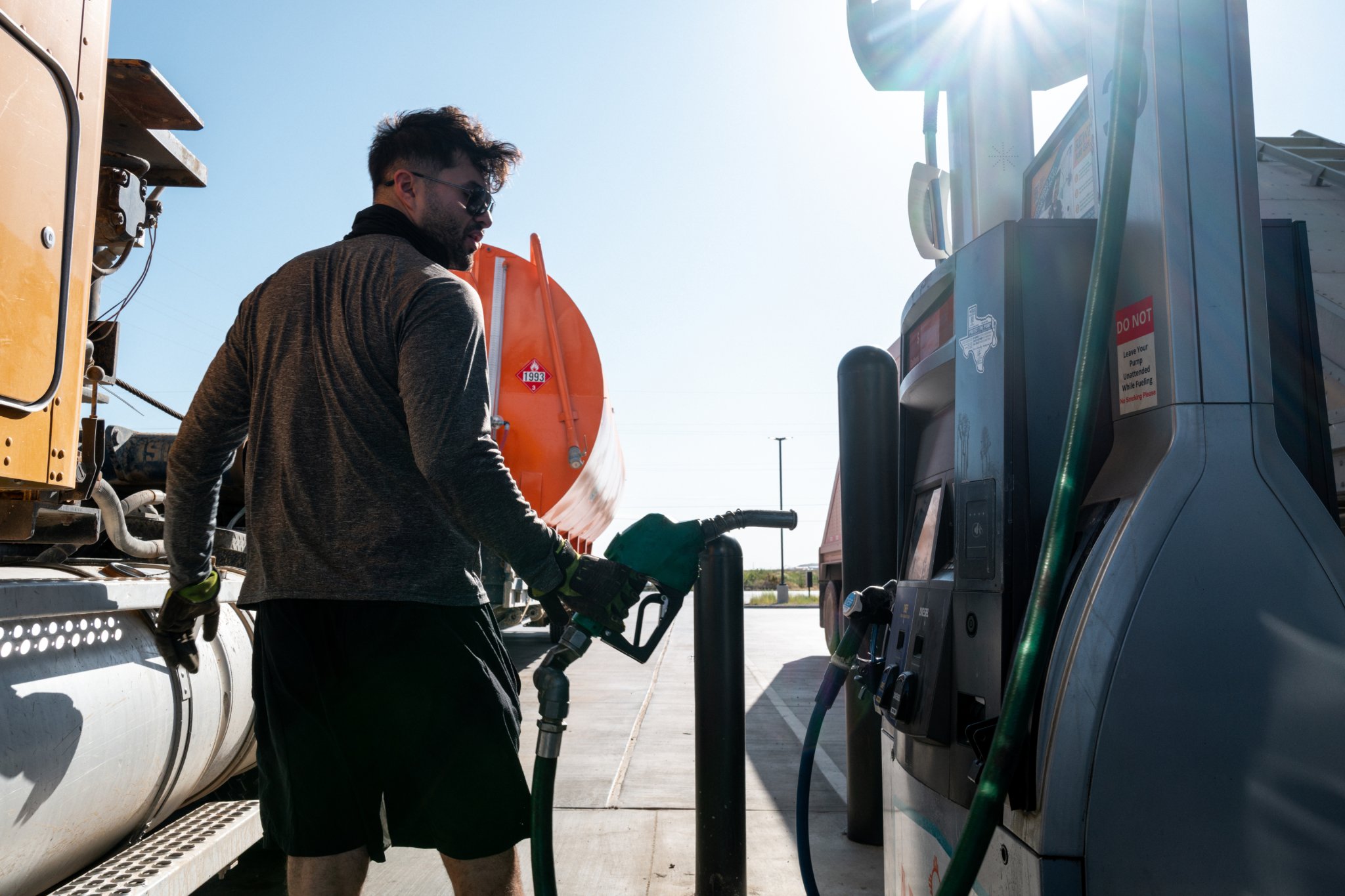 Man fueling a large truck at a gas station with a Texas sticker