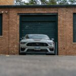 Silver Ford Mustang Mach 1 parked in front of brick garage