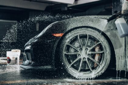 A person spraying soapy foam onto a black sports car in a garage