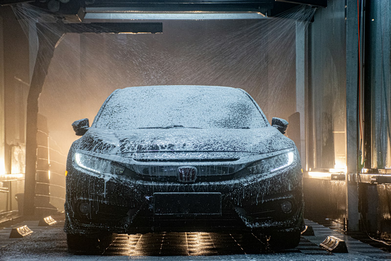Black car covered in foam inside an automated car wash