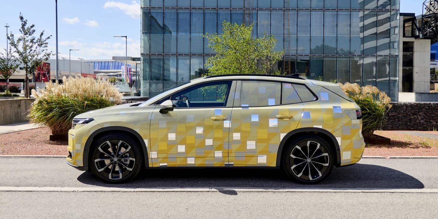 Camouflaged Volkswagen electric SUV prototype parked on a street in side profile