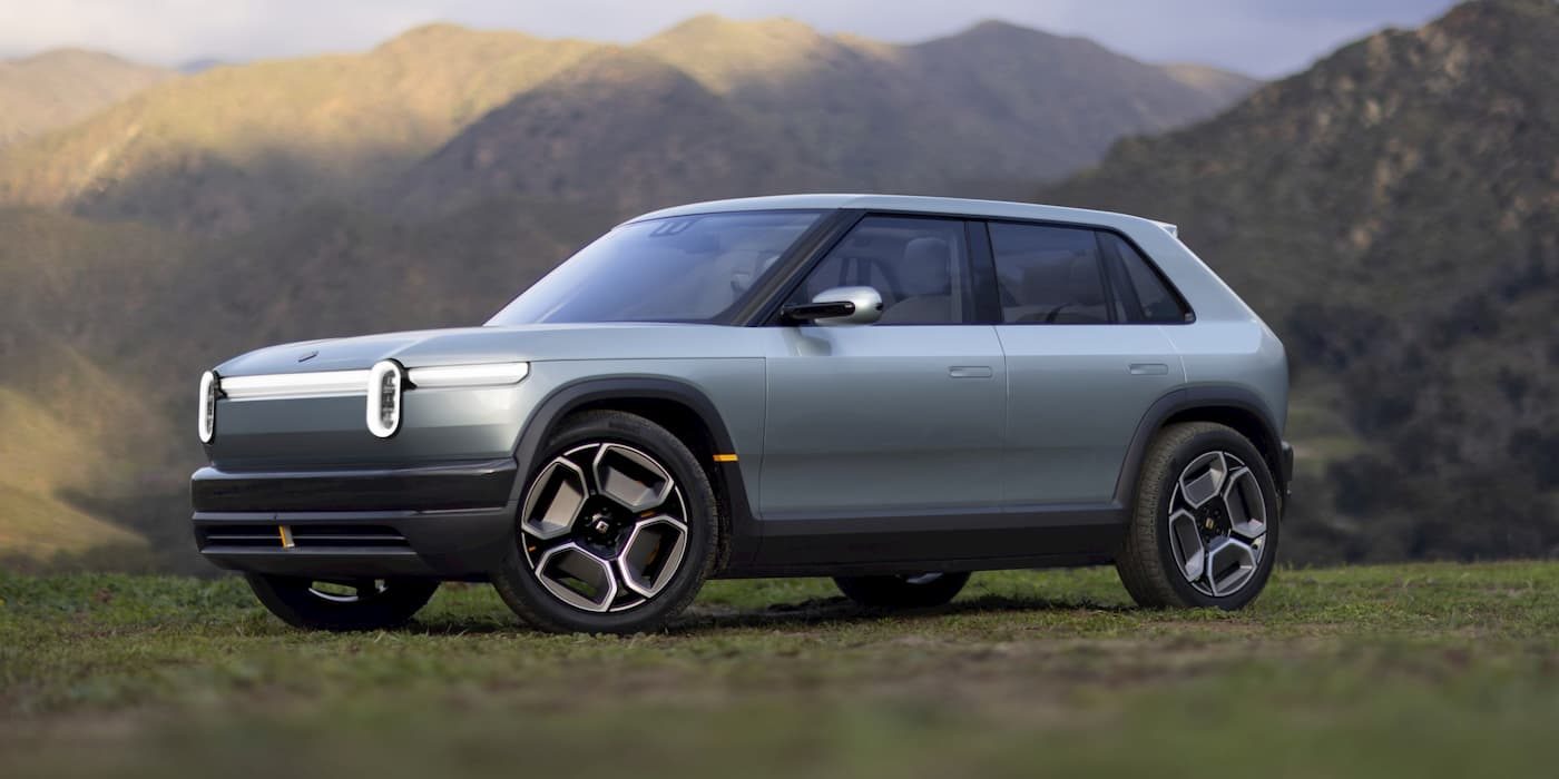 Rivian R3 electric SUV parked on grassy hillside with mountains behind