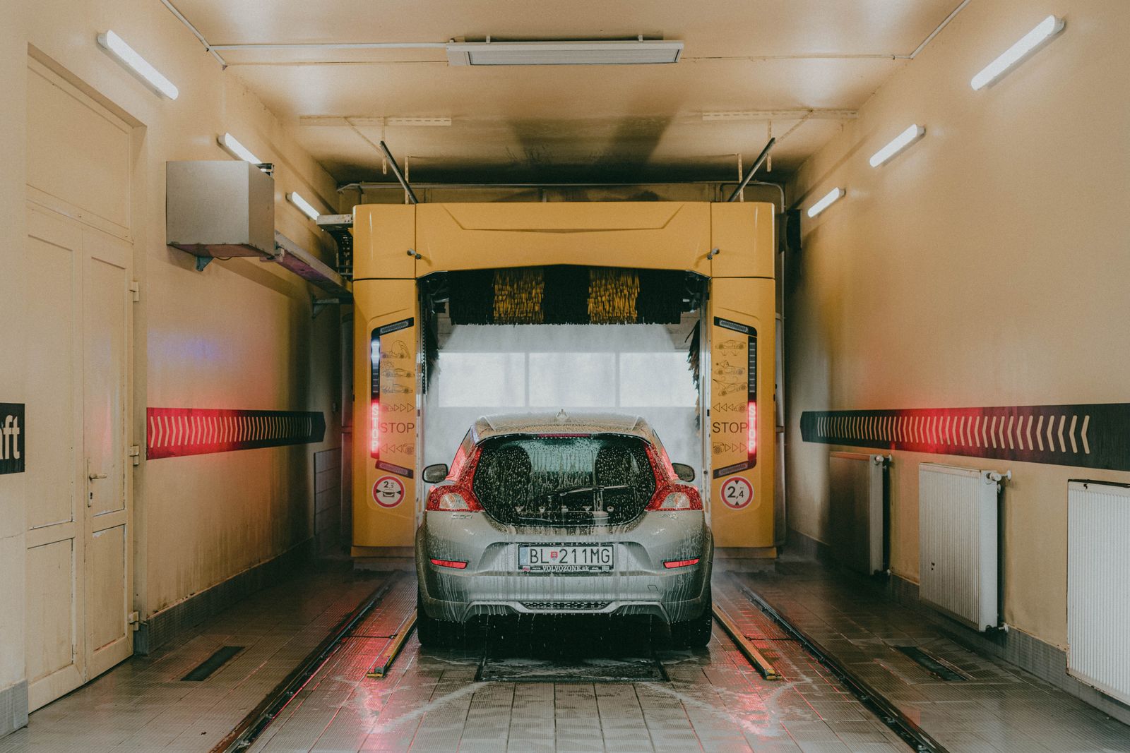 Car inside automatic car wash tunnel with yellow machinery and water spray