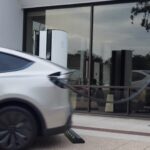 White Tesla driving away while still plugged into a Supercharger cable