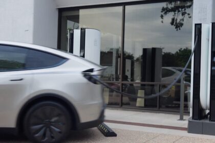 White Tesla driving away while still plugged into a Supercharger cable