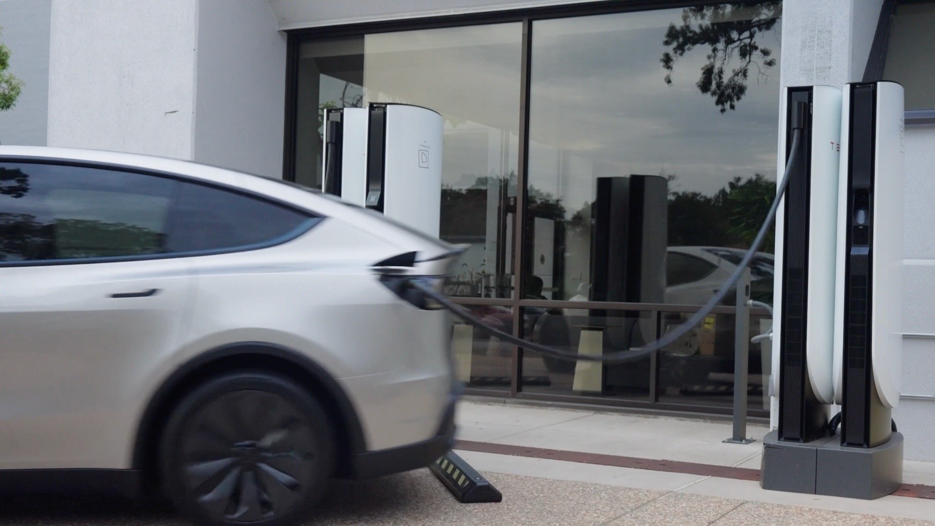 White Tesla driving away while still plugged into a Supercharger cable