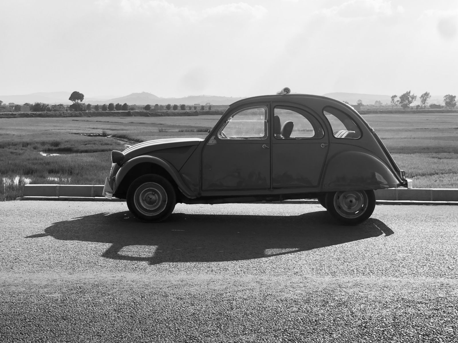 Classic Citroen 2CV parked in profile beside rural fields