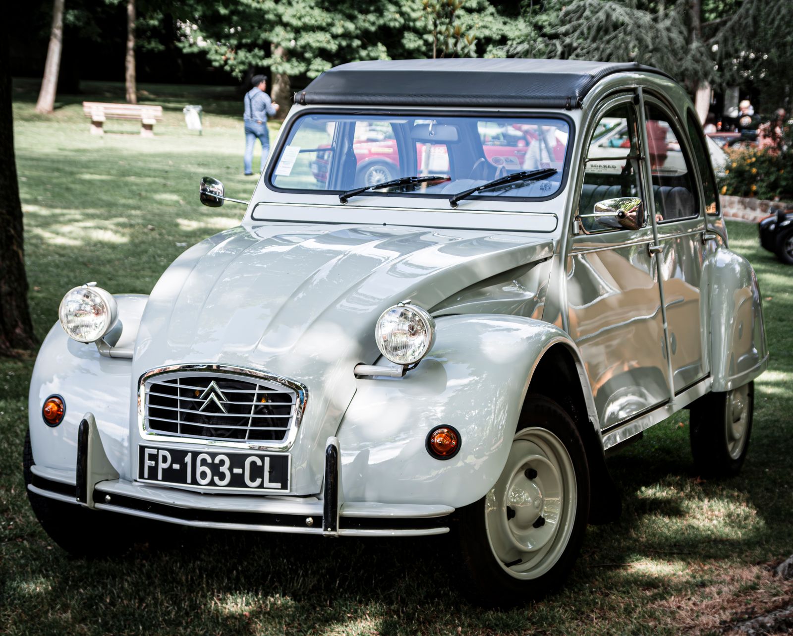 Classic light gray Citroen 2CV parked on grass at an outdoor event