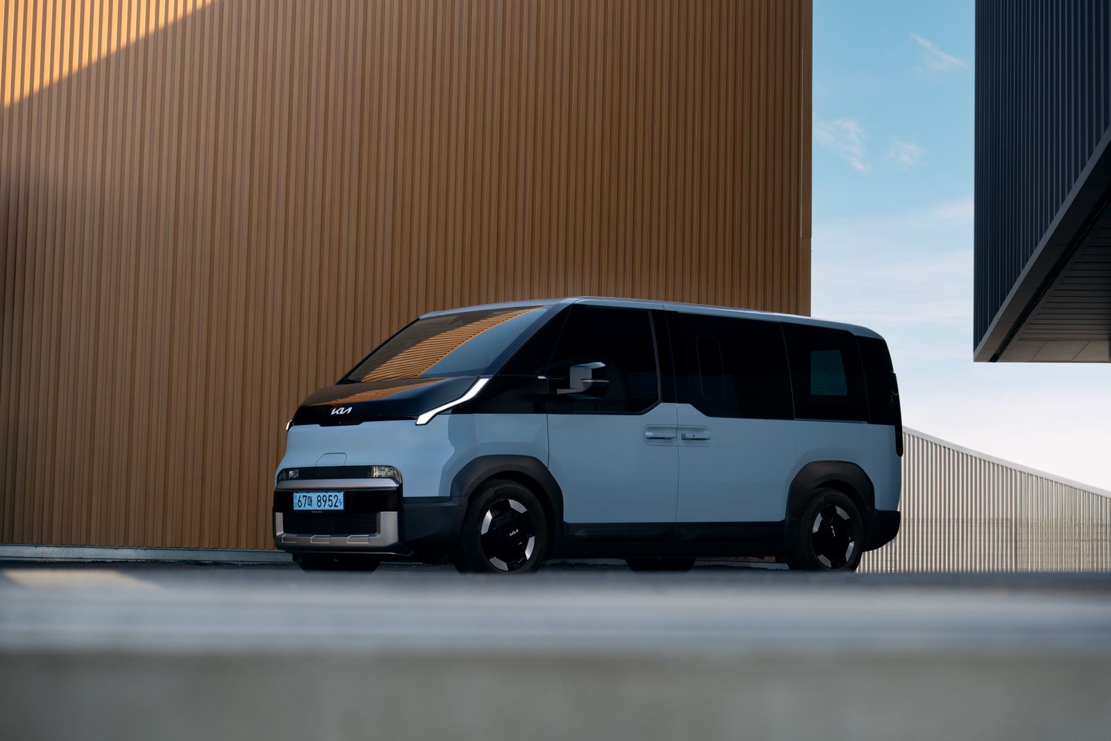 Light blue Kia electric van parked beside modern wooden building