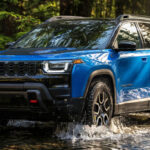 Blue Jeep Cherokee Trailhawk splashing through water on off-road trail