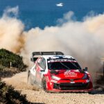Rally car speeding on dusty coastal road during WRC event