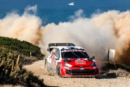 Rally car speeding on dusty coastal road during WRC event