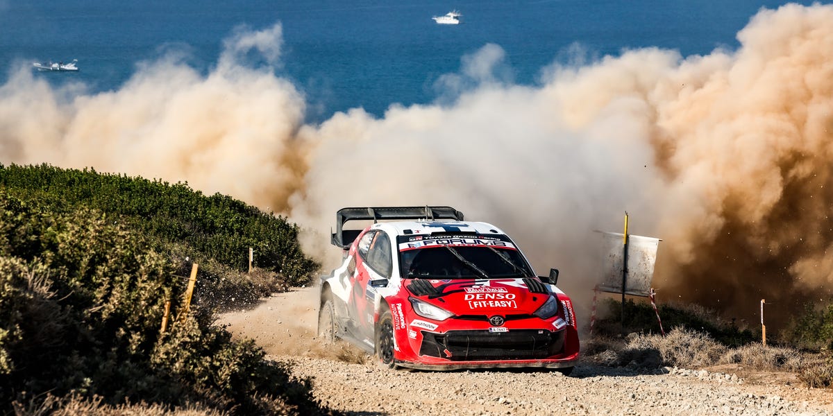 Rally car speeding on dusty coastal road during WRC event