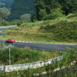 Red car driving on a winding race track through green hills