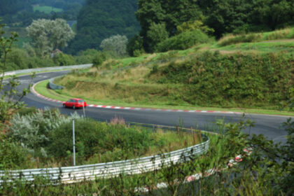 Red car driving on a winding race track through green hills