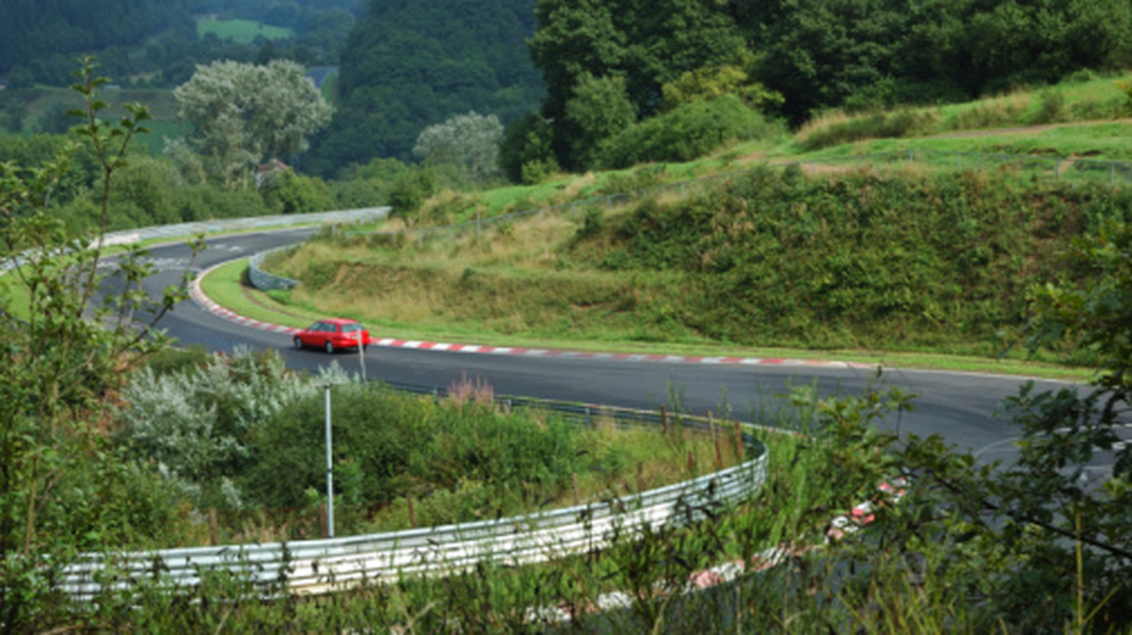 Red car driving on a winding race track through green hills