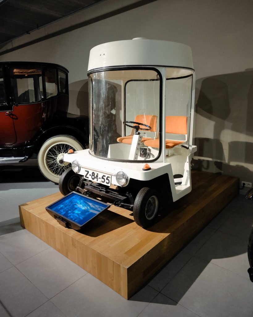 White Witkar electric car on museum display with wooden platform