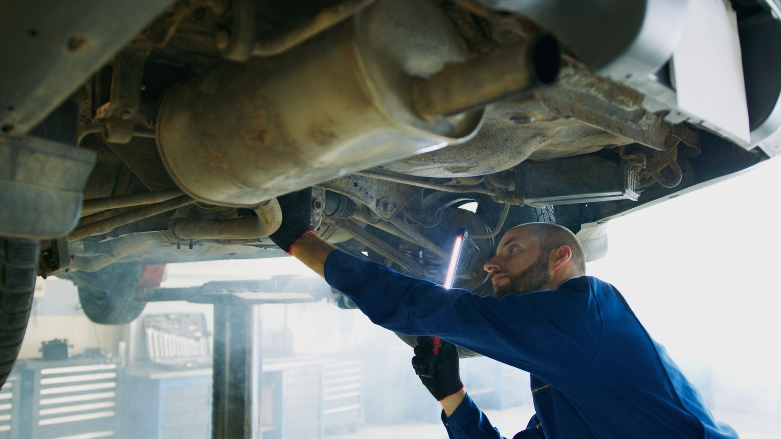 Mechanic inspecting underside of car with flashlight in workshop